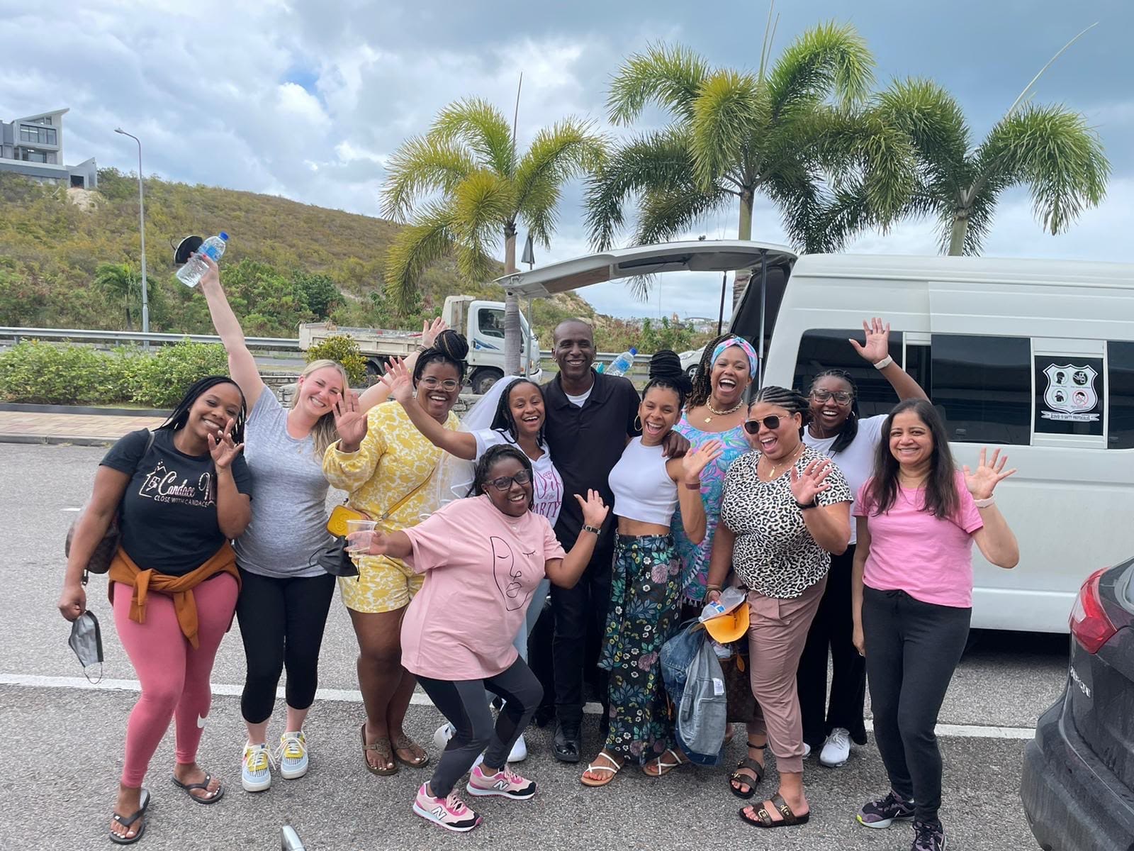 A large happy group of guests waving beside the white Toyota HiAce